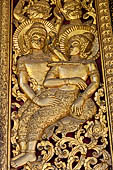 Wat Xieng Thong temple in Luang Prabang, Laos. Detail of a wooden door of the sim with gilded carvings on a red background. 